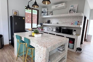 A kitchen with a speckled countertop, bar stools, a refrigerator, and a microwave. - Villa NaRa Chaam (Cha-am)
