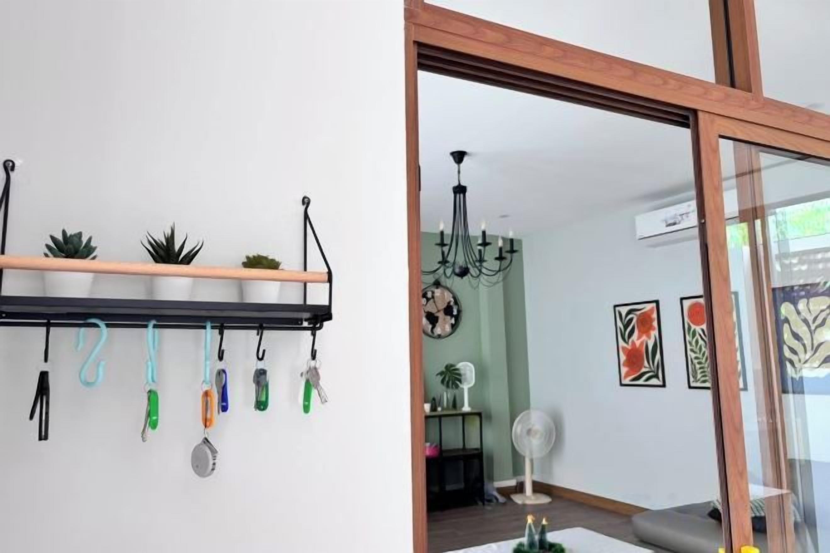 Una habitación con un estante en la pared que sostiene llaves y una planta pequeña, un ventilador de techo y una ventana con vistas al exterior.
