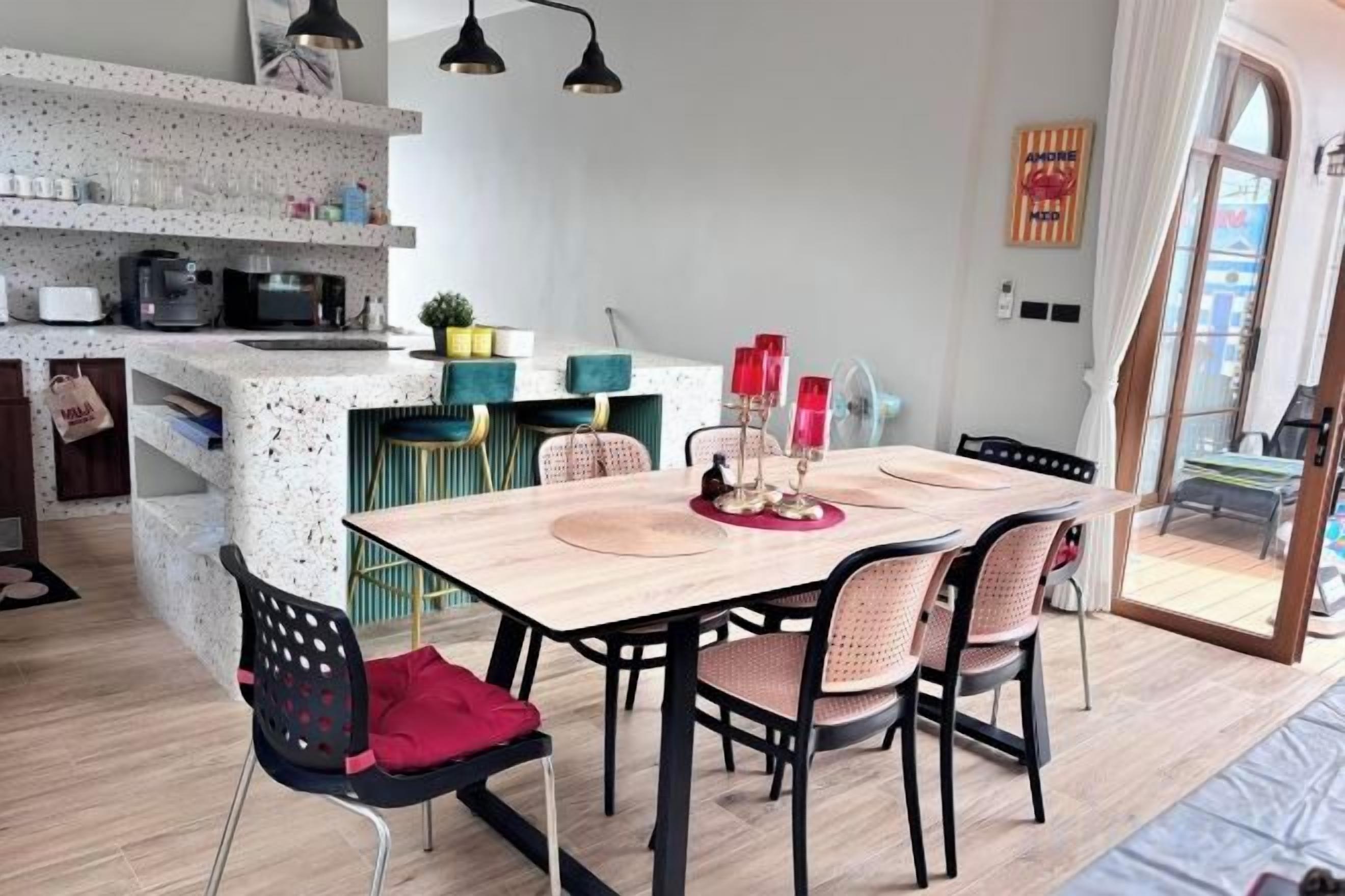 Un comedor con una mesa y sillas de madera, una cocina al fondo y una vista a través de un vano.