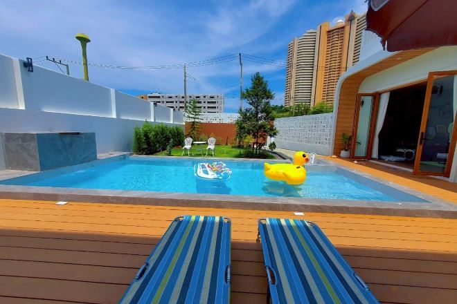 Une piscine avec des chaises longues, un canard gonflable jaune et une vue sur un bâtiment moderne.