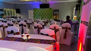 A banquet hall with rows of tables, each covered with white tablecloths and adorned with floral centerpieces. - ALLENS HOTEL (Kapsabet)