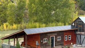 A rustic wooden cabin with a metal roof, a small porch, and a garage. - Yun-Shui Garden 
Where Clouds Drift, Water Flows (Durango)