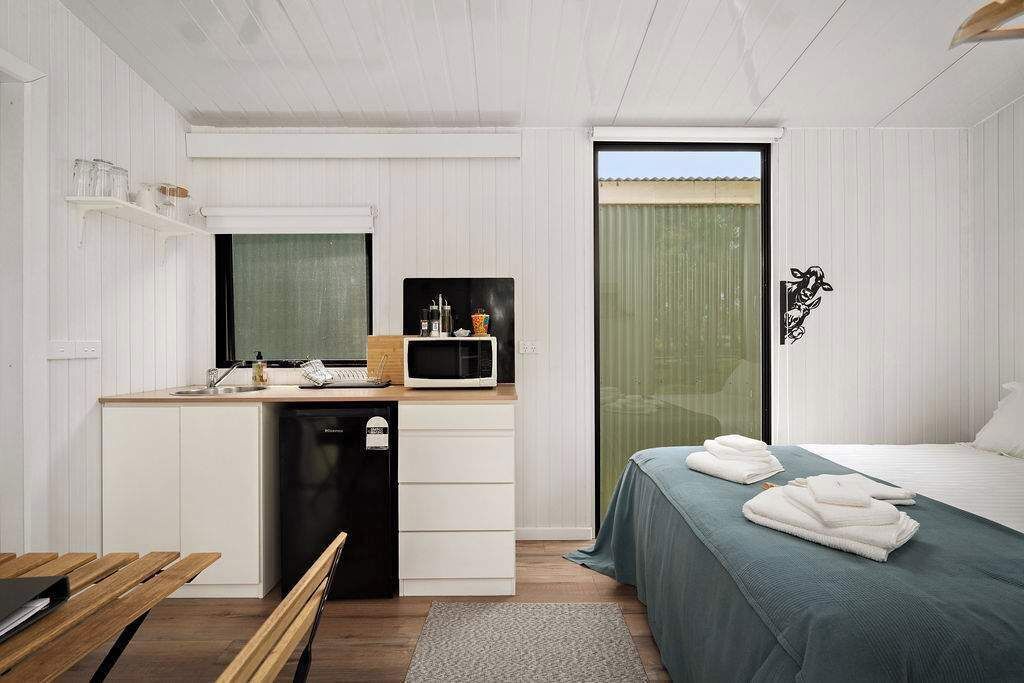 A compact bedroom with a bed, bedside table, and a small kitchenette area including a microwave and a sink.