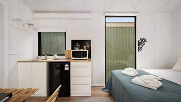 A compact bedroom with a bed, bedside table, and a small kitchenette area including a microwave and a sink.