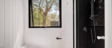A bathroom with a white toilet, a window with a view of trees, and a black shower door.