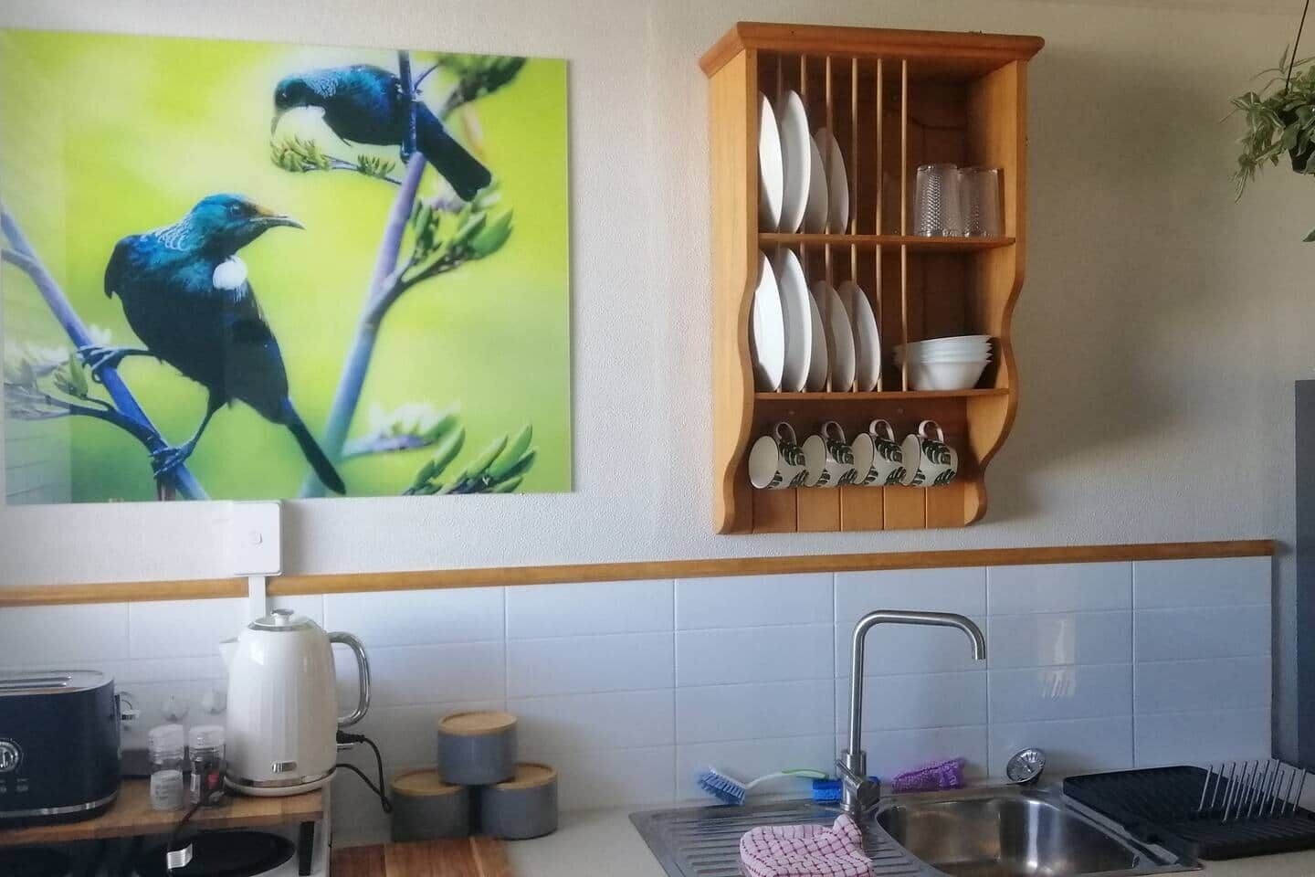 Een keuken met een spoelbak, een waterkoker en een plank met servies.