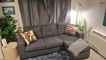 Un sofá seccional gris con una manta, una mesita auxiliar y una planta en maceta.