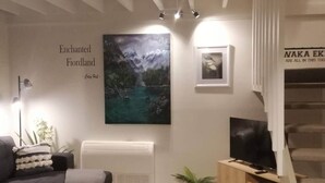 Un salón con un cuadro grande de un paisaje montañoso, un sofá, un televisor y un radiador.
