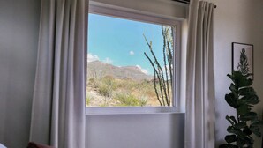 Une chambre dotée d’une grande fenêtre donnant sur un paysage désertique et des montagnes.