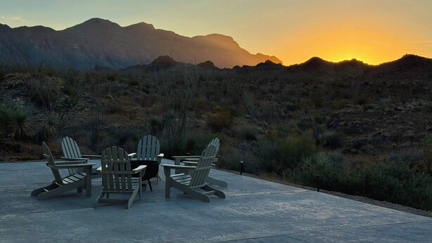 Une terrasse dotée de fauteuils Adirondack et d’une table, offrant une vue sur un paysage désertique avec des montagnes à l’horizon.