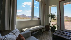 Une pièce avec un banc, une plante en pot et une vue sur un paysage désertique, visible à travers de grandes fenêtres.