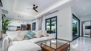 A modern living room with a sectional sofa, a glass coffee table, and a ceiling fan. - Two Flamingo Villa 1 (Phuket)