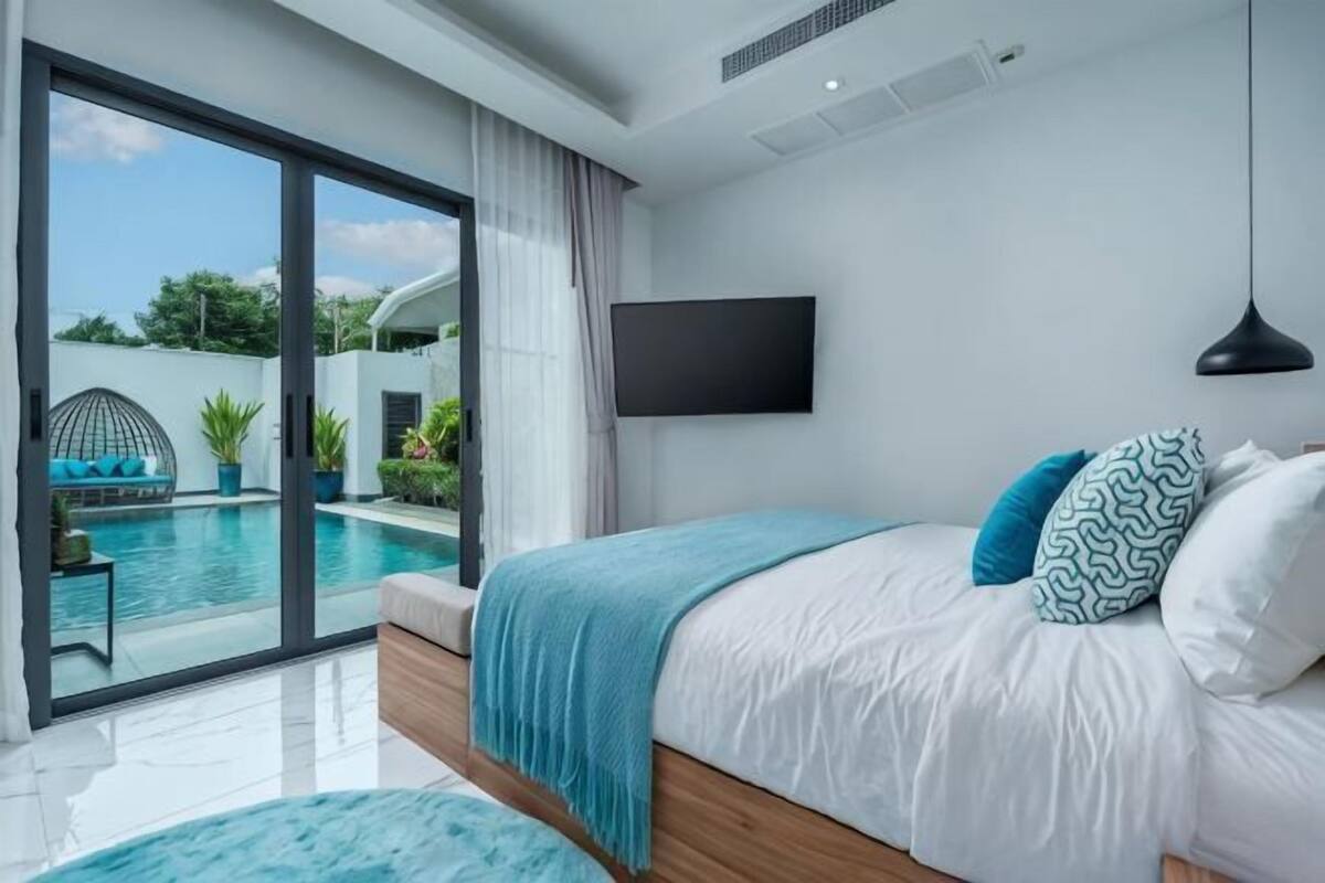 A bedroom with a bed, a TV, a pool view, and a sliding door.