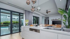A modern kitchen with a large island, a built-in dishwasher, and a dining area with a sofa and table. - Two Flamingo Villa 1 (Phuket)