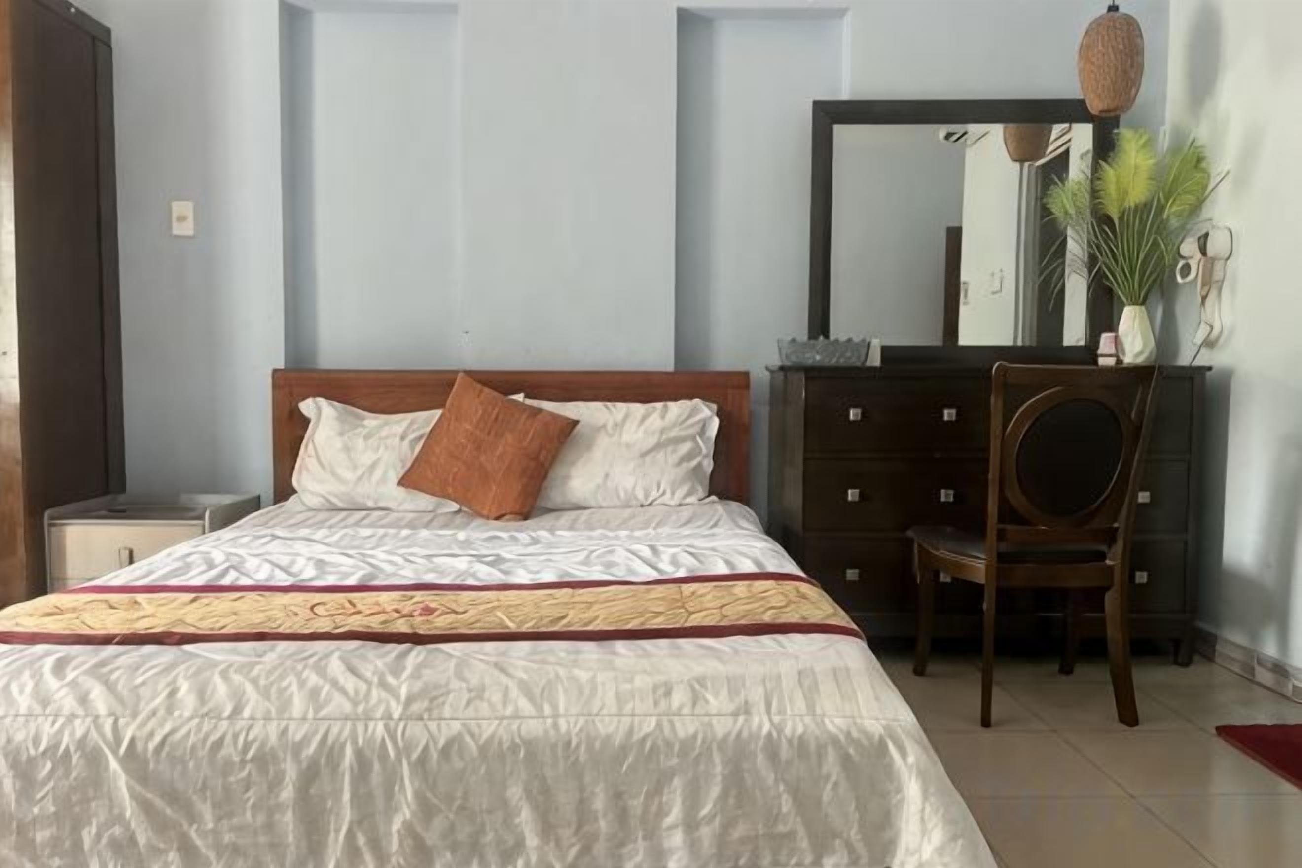 A bedroom with a bed, a dresser, a chair, and a mirror.