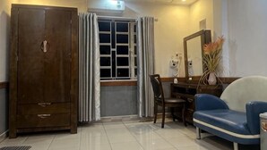 Quarto com guarda-roupa, janela com cortinas, escrivaninha com cadeira, sofá e um vaso de planta.