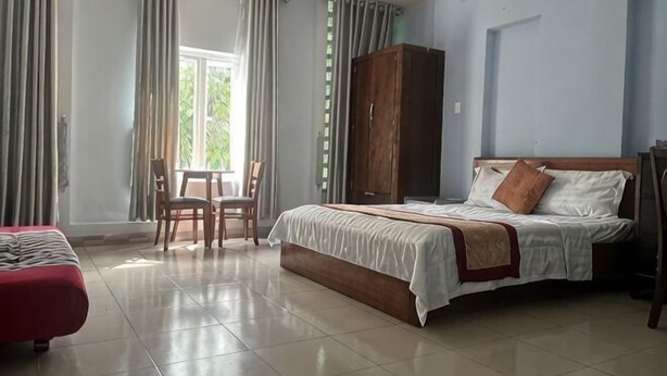 Quarto com cama, guarda-roupa de madeira, sofá vermelho e uma pequena mesa com cadeiras.