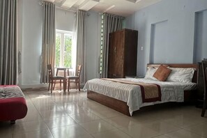 A bedroom with a bed, a wooden wardrobe, a red sofa, and a small table with chairs.