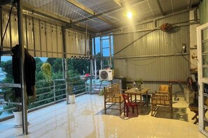A spacious indoor area with a high ceiling, a table with chairs, a potted plant, and a large window providing a view of greenery outside. - Hotel KunLun (Thi xa Ben Cat)