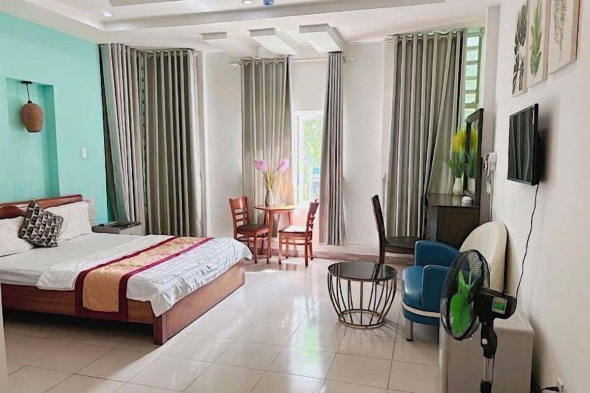 A hotel room with a bed, a small table with chairs, a fan, and a TV mounted on the wall.