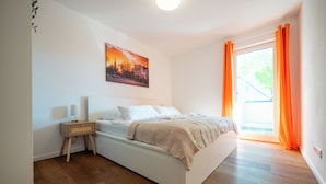 Une chambre à coucher avec un lit, une table de chevet, une lampe et une fenêtre avec des rideaux.