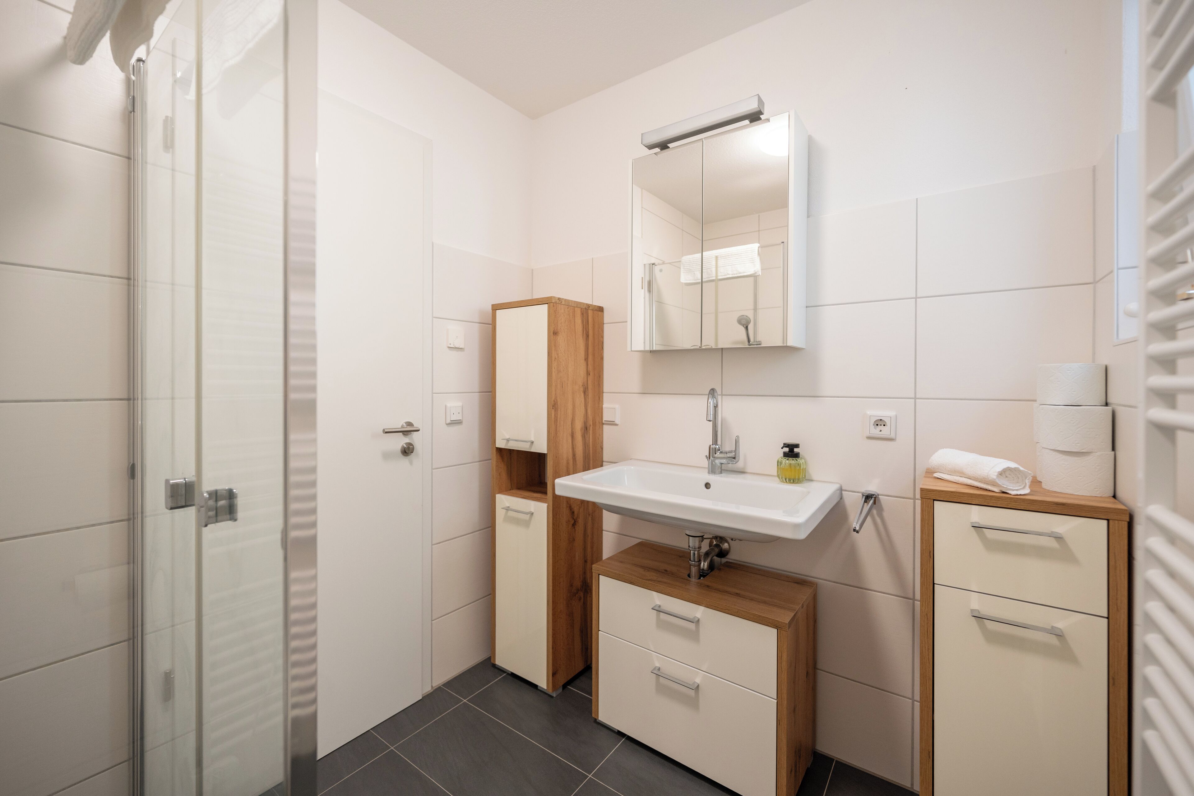 A modern bathroom with a glass shower enclosure, a wooden vanity with a sink, and a mirror above the mirror cabinet.