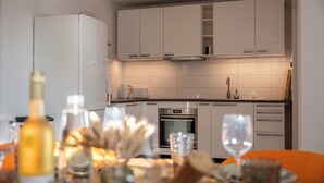 Une cuisine moderne avec des armoires blanches, un four encastré et un coin repas agrémenté de chaises orange et d’une table dressée pour deux personnes.
