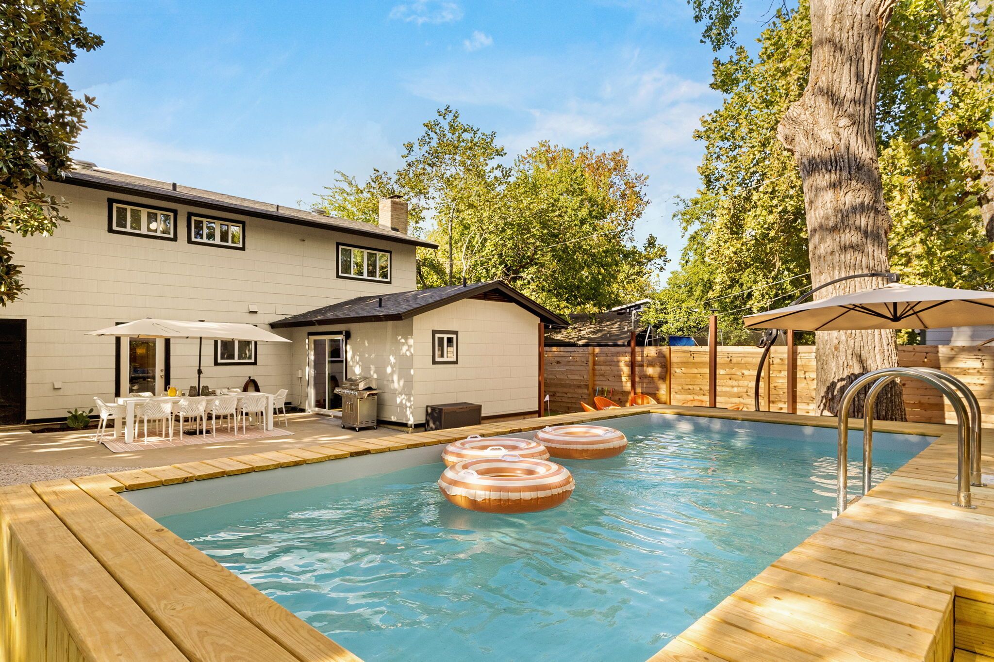 A swimming pool with wooden deck, inflatable rings, and outdoor seating.