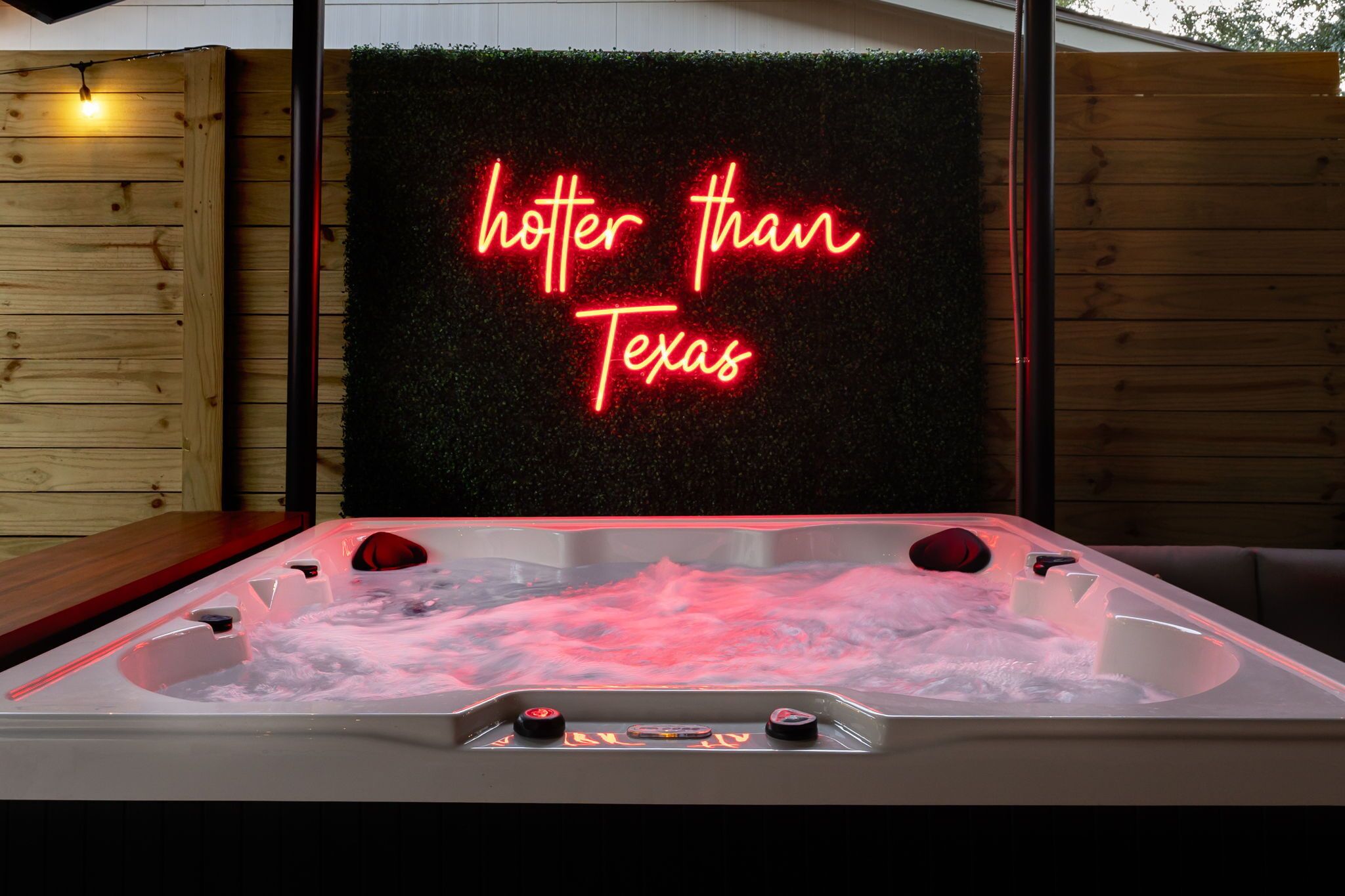 A hot tub with a neon sign reading "hotter than Texas" in the background.