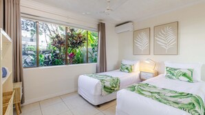 Una habitación con dos camas, una ventana con cortinas, un ventilador de techo y aire acondicionado instalado en la pared.
