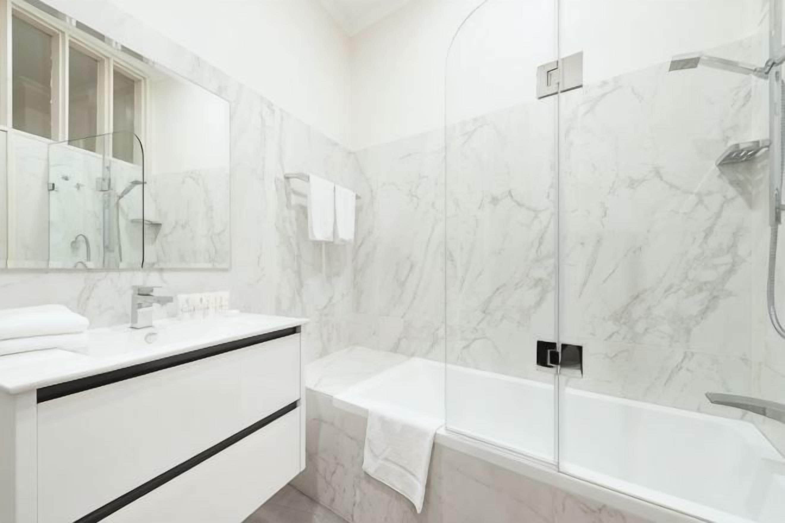 A modern bathroom with a marble wall, a bathtub, a shower enclosure, and a vanity with a mirror.