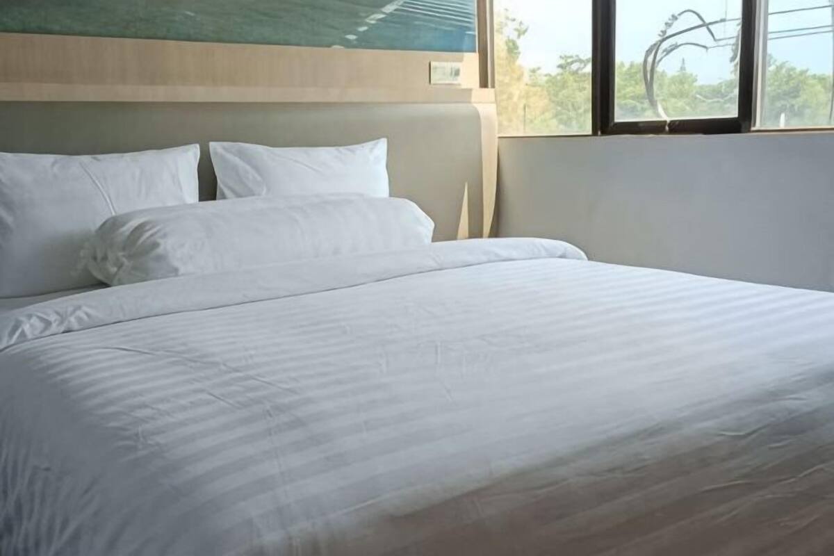 A bed with white bedding, a wooden headboard, and a window with a view of trees.
