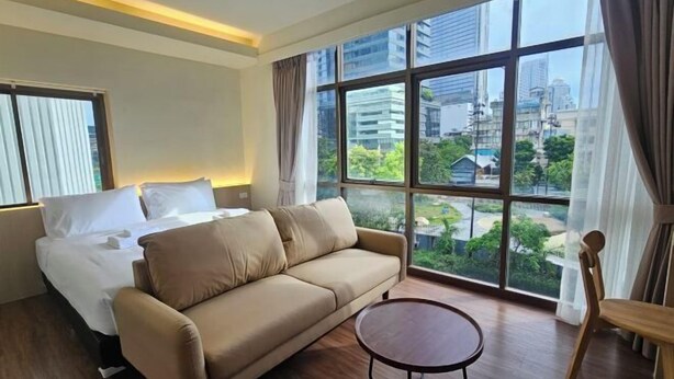 Ein Hotelzimmer mit einem Bett, einer Couch, einem runden Tisch und großen Fenstern mit Blick auf die Stadt.
