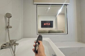 Een badkamer met een douche, een bad en een spiegel die een bordje met 'NETFLIX' weerkaatst.