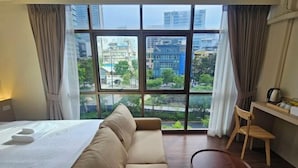 Ein Hotelzimmer mit Bett, Sofa, einem kleinen Tisch und Blick auf die Stadt durch große Fenster.