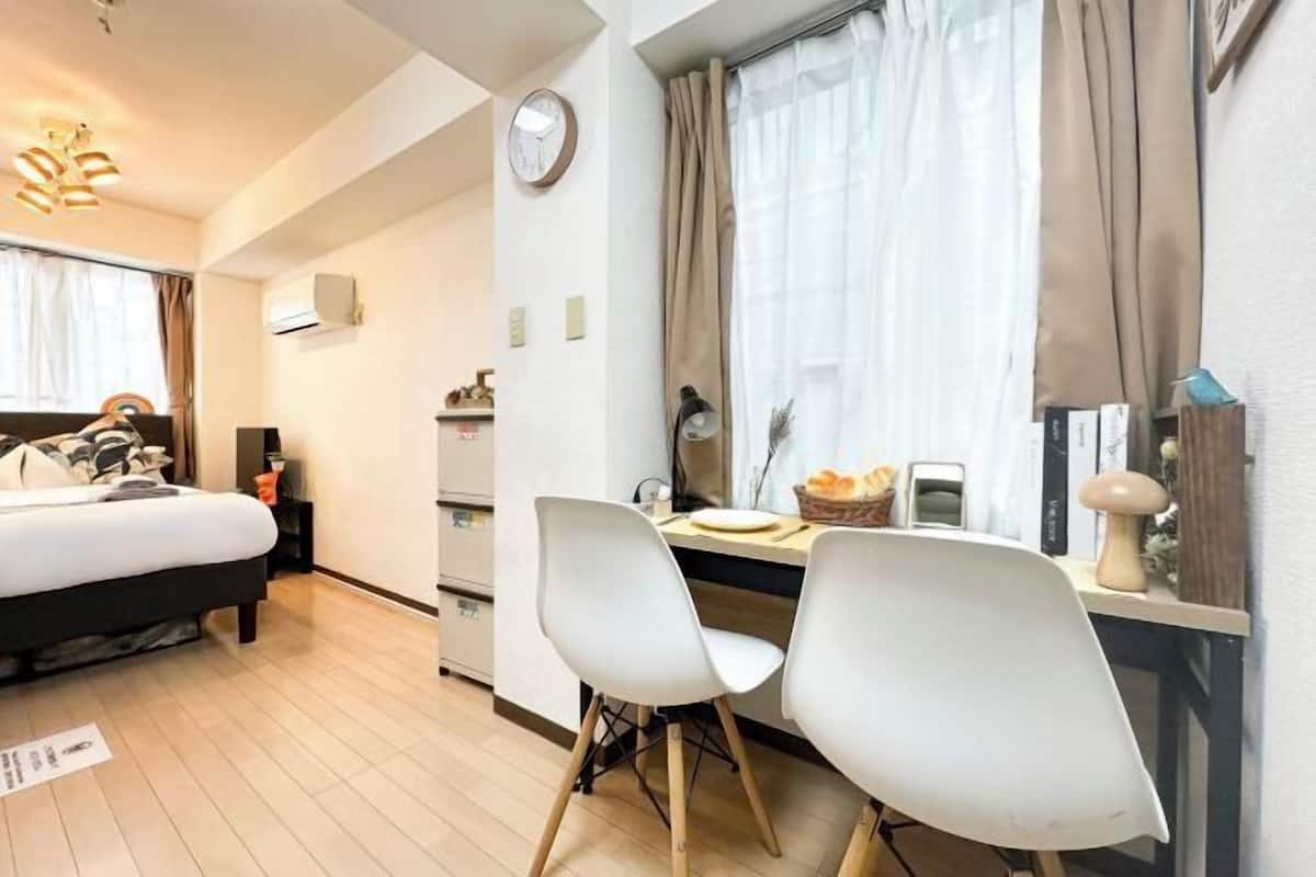 Habitación de hotel con cama, escritorio con dos sillas, un reloj y ventana con cortinas.