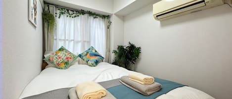 A hotel room with a bed, two pillows, a blue bedspread, and an air conditioning unit on the wall.