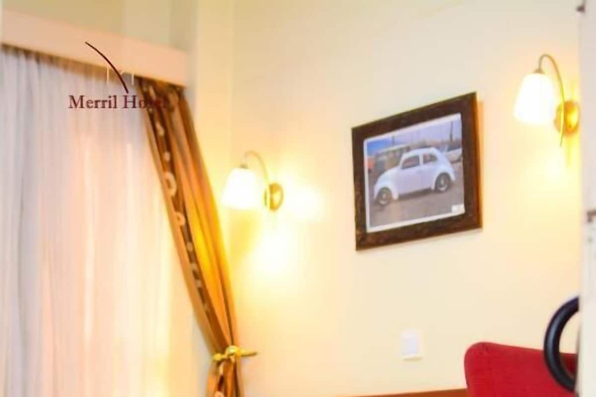 A hotel room with a bed, a red chair, a framed picture on the wall, and a curtain.