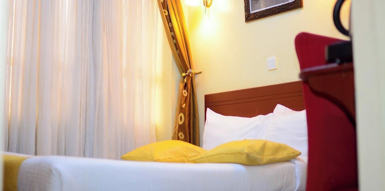 A hotel room with a bed, a red chair, a wall-mounted lamp, and a framed picture on the wall.