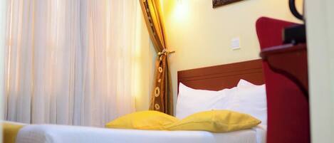A hotel room with a bed, a red chair, a wall-mounted lamp, and a framed picture on the wall.