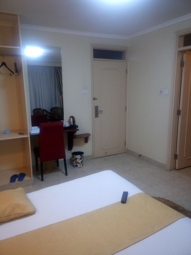 A small, sparsely furnished room with a bed, a desk, a chair, and a wardrobe.