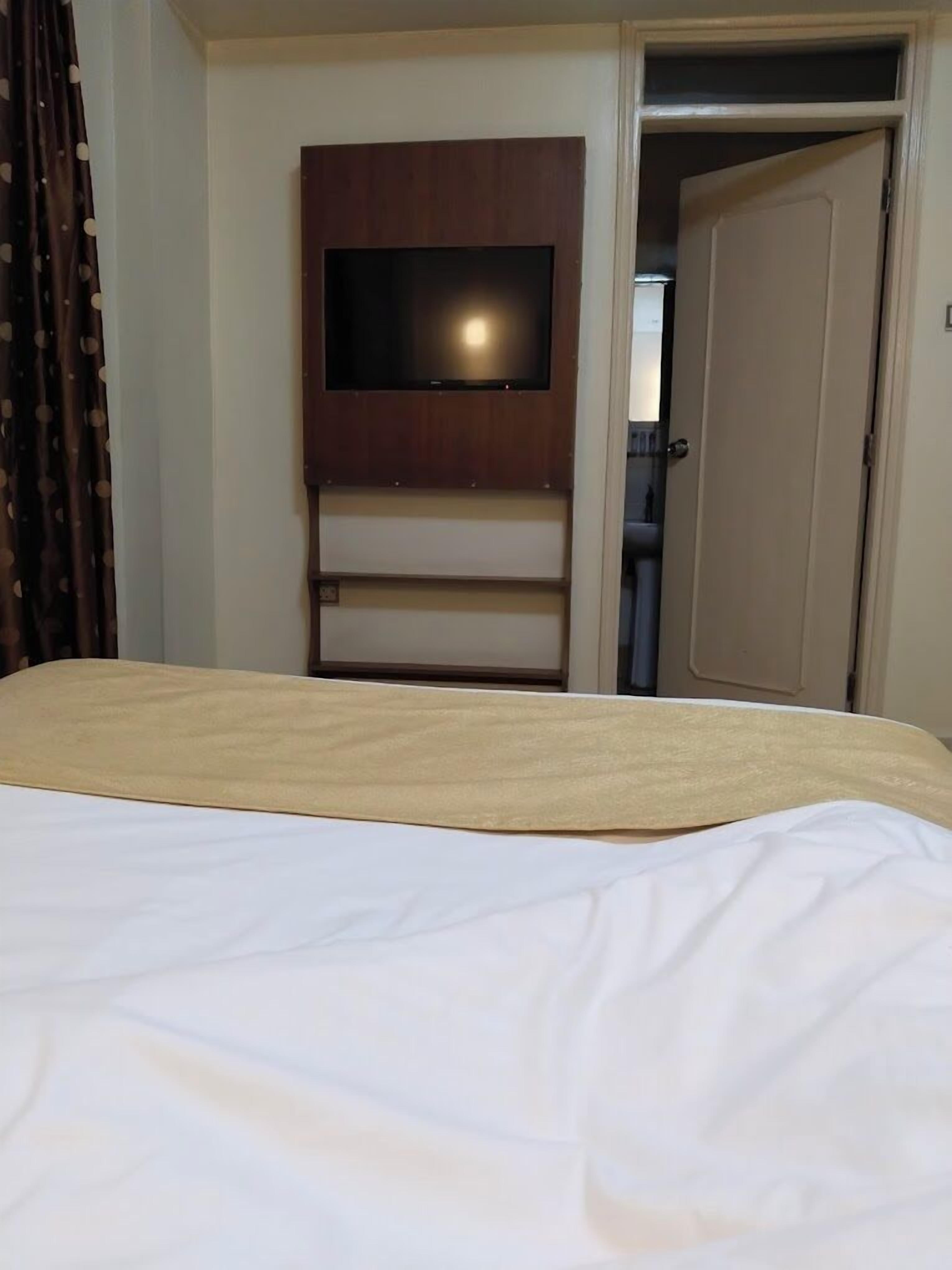 A hotel room with a bed, a television mounted on a wooden cabinet, and a door leading to another room.