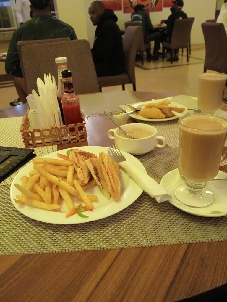 Une table à manger avec une assiette de frites, un sandwich et un verre de café. On y trouve également des condiments et des couverts.