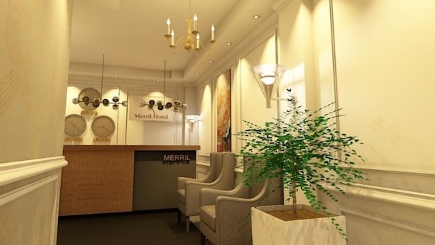 Et hotellets reception område med et skrivebord, stole, en lysekrone, vægur og en potteplante.
