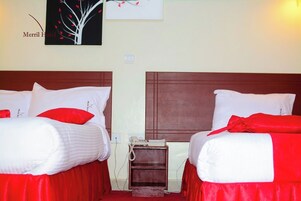 Camera d'albergo con due letti, ognuno con biancheria da letto bianca e dettagli rossi. Una pittura raffigura un albero sulla parete, e un piccolo comodino in legno con un telefono tra i letti.