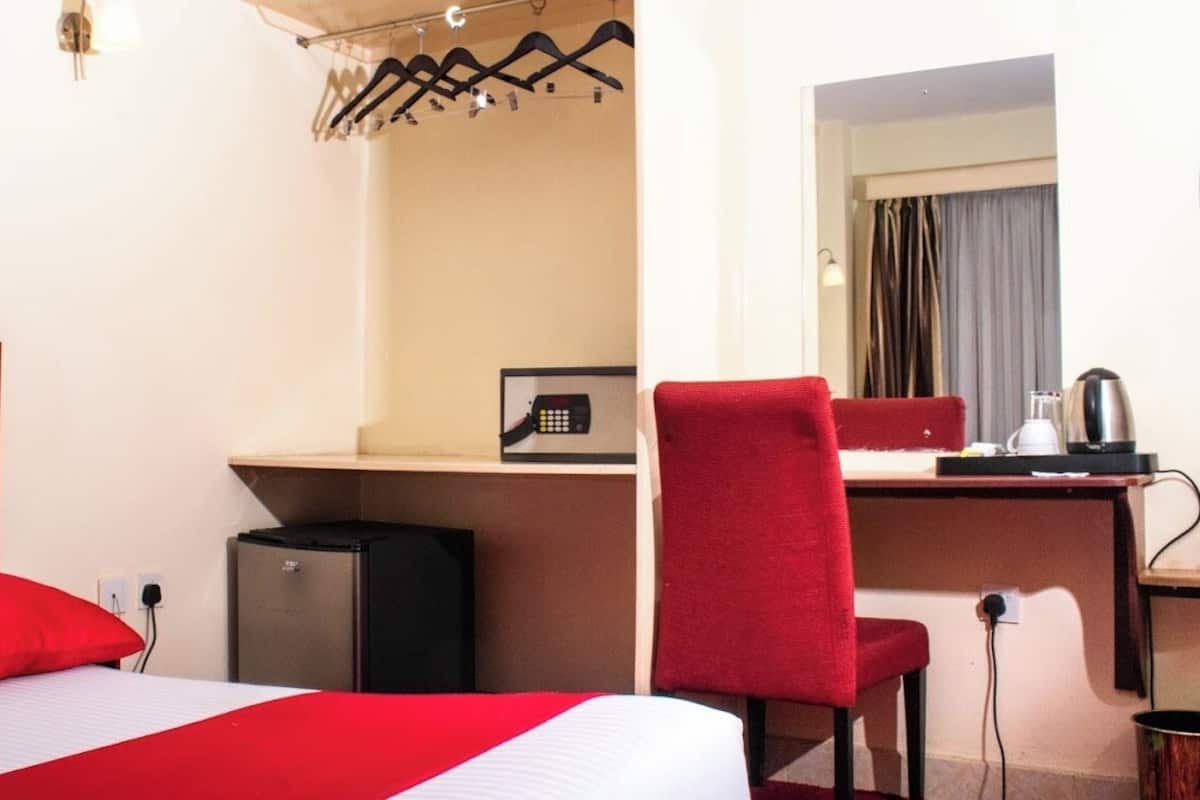 A hotel room with a bed, a desk, a chair, a small refrigerator, a microwave, and a kettle.