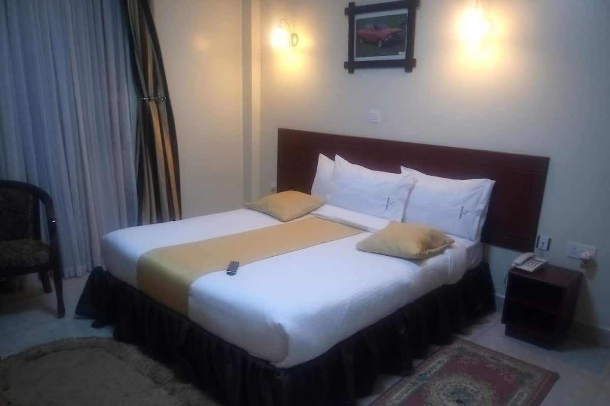 A hotel room with a large bed, a bedside table with a phone, and a chair.