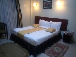 A hotel room with a large bed, a bedside table with a phone, and a chair.