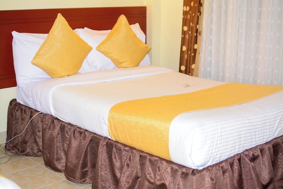 A neatly made bed with white and yellow bedding, a brown skirted bed base, and a wooden headboard.