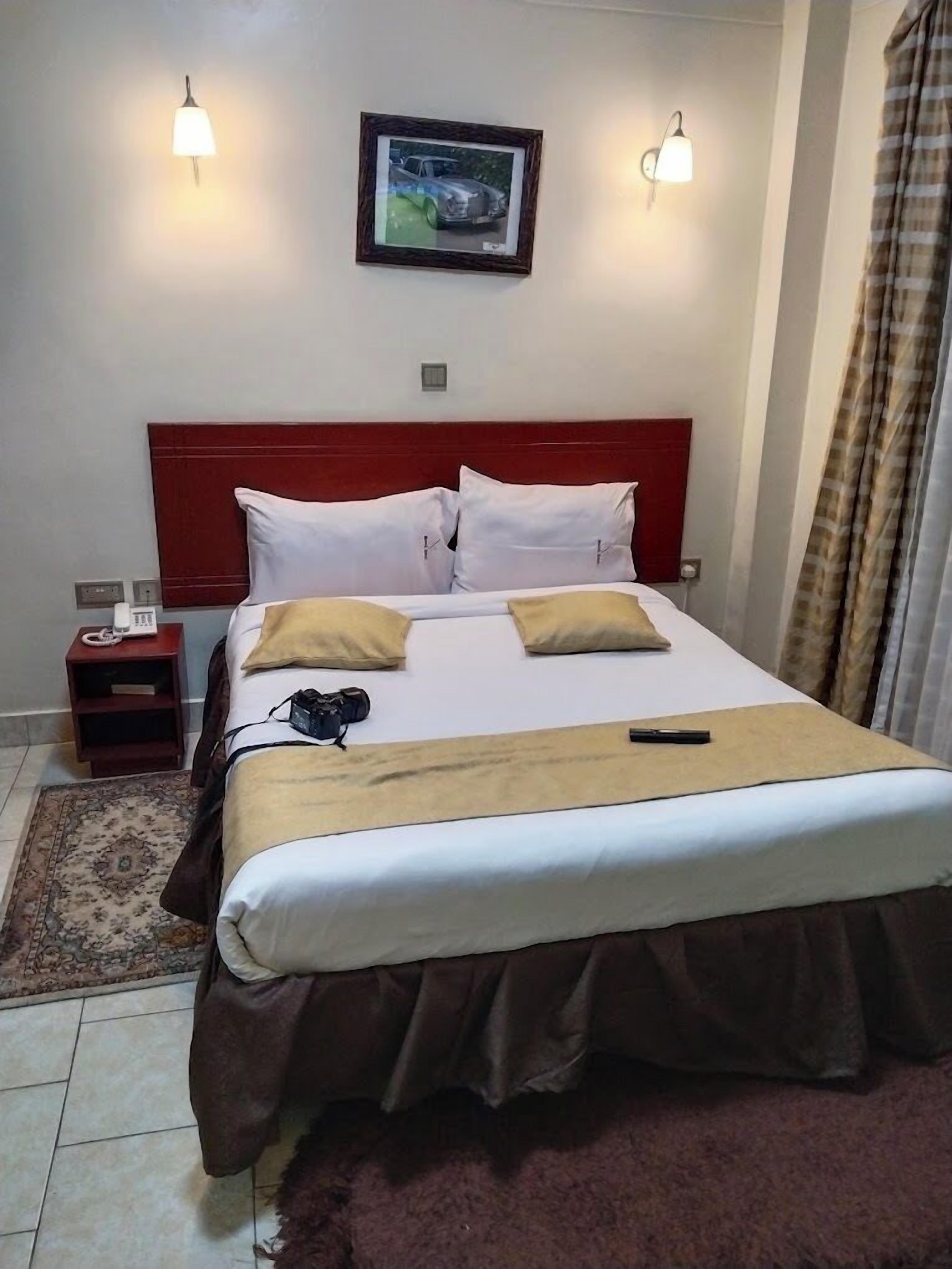 A neatly made bed with white and brown bedding, a red headboard, and two wall-mounted lights.